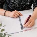 Eine Frau setzt den Füller an und schreibt in ein noch leeres, kariertes Notizheft.