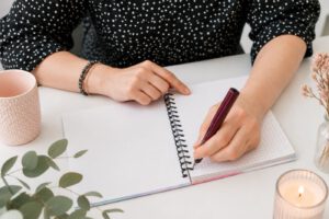 Eine Frau setzt den Füller an und schreibt in ein noch leeres, kariertes Notizheft.